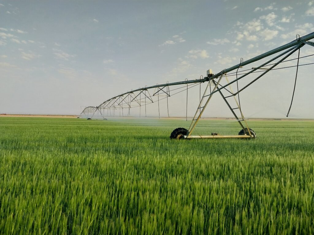 A pivot irrigation system waters lush green crops in an expansive rural field.